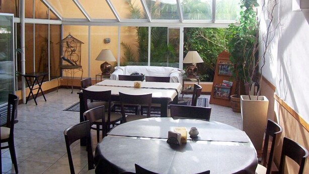 A conservatory with a dining area, a sofa, and a lamp. - Hotel del Rey (La Plata)