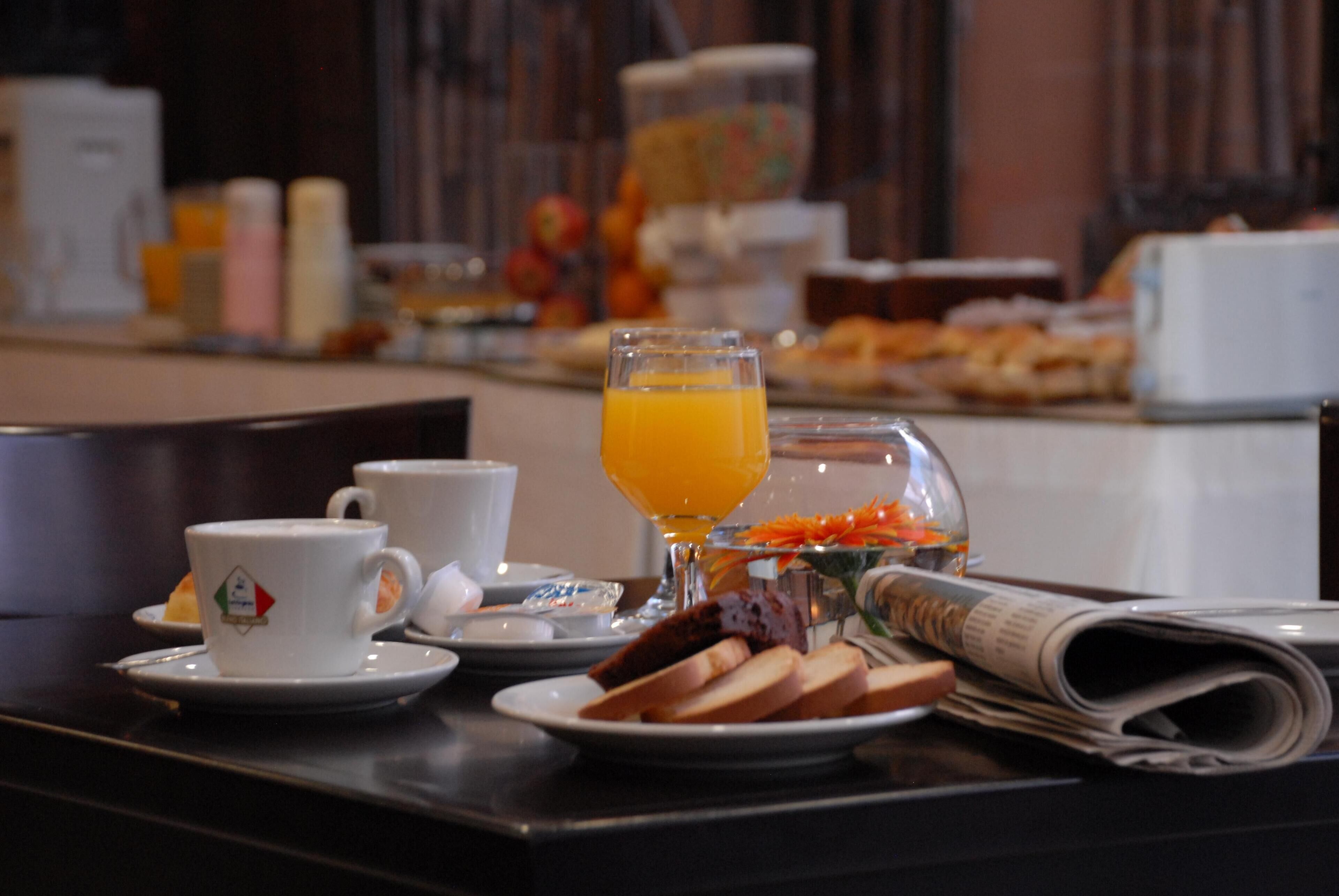 A breakfast table with a cup, glass of orange juice, bread, and a newspaper.