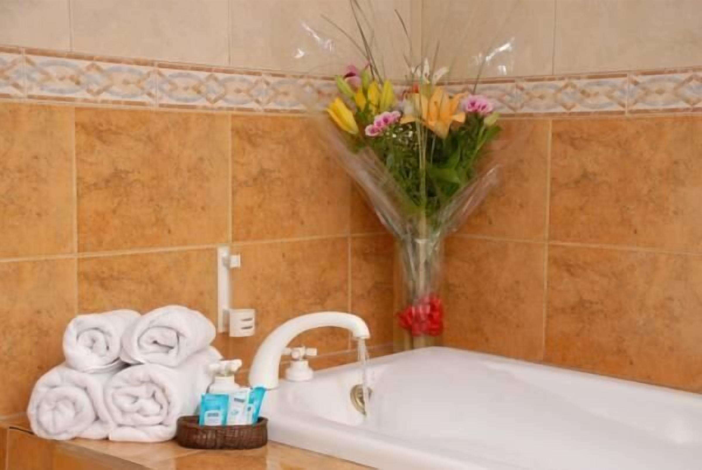 Ett badrum med ett vitt badkar, hoprullade handdukar, hygienartiklar och en bukett blommor.