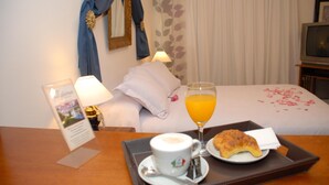 A hotel room with a bed, a tray with breakfast including a croissant and orange juice, a coffee cup, and a pillow. - Hotel del Rey (La Plata)