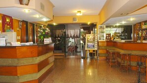 A hotel lobby with a reception desk, a bar area with stools, and a display of framed pictures. - Hotel del Rey (La Plata)