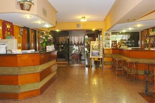 Un vestíbulo de hotel con una recepción, una zona de bar con taburetes y una exposición de cuadros enmarcados.