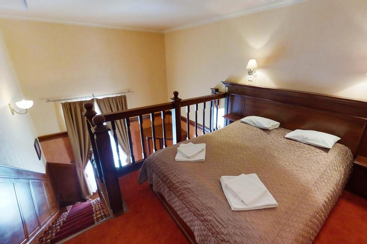 A hotel room with a bed, two bedside lamps, a wooden headboard, and a view of the staircase.