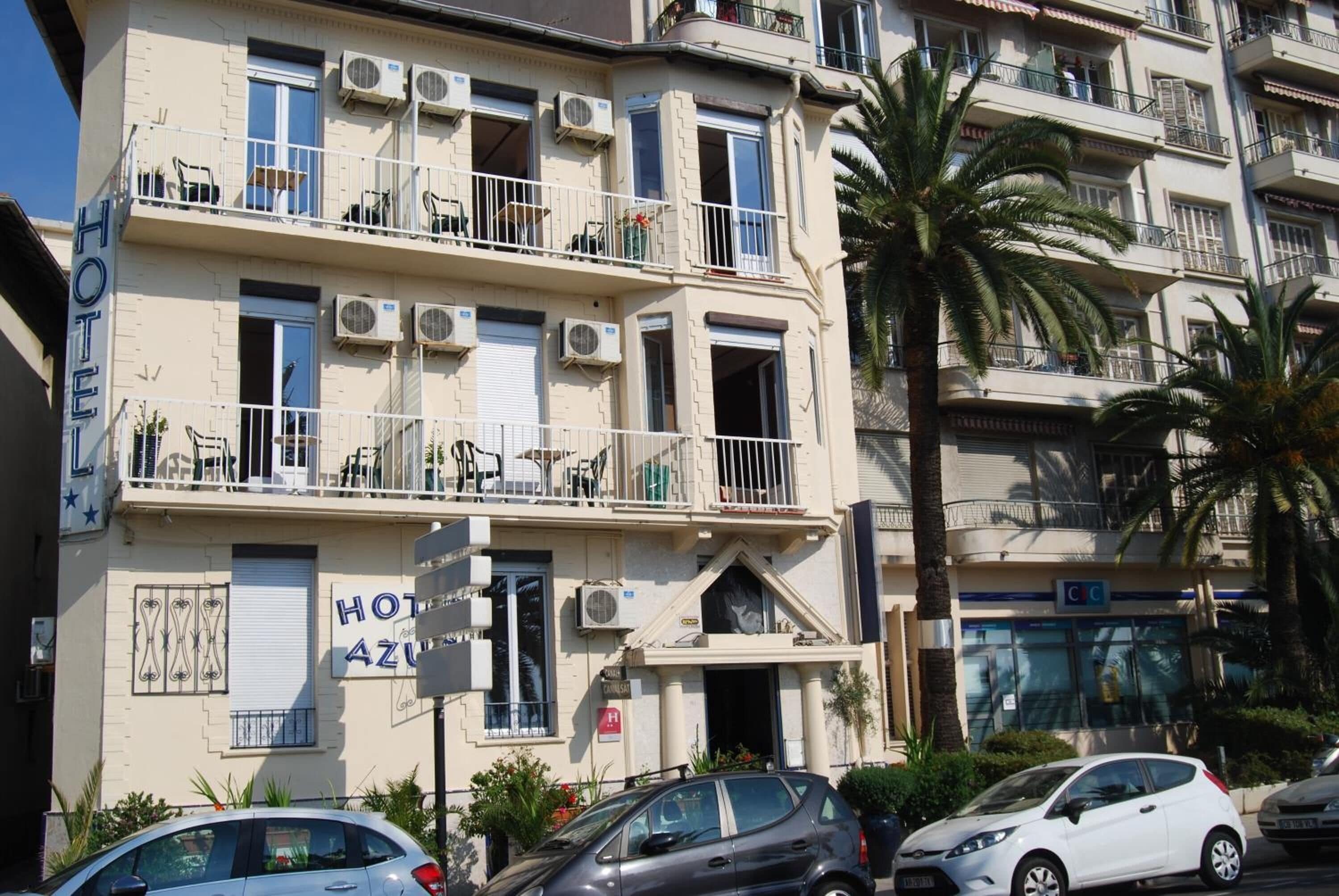 Un hôtel à plusieurs étages doté de balcons, de climatiseurs et d’une enseigne indiquant le nom de l’hôtel : « HOT AZU ».