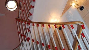 A spiral staircase with red and white balusters, a round window at the top, and wall-mounted lights. - Azur (Nice)