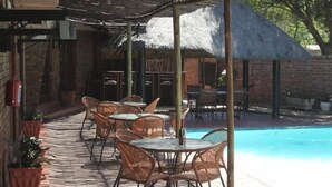 Un patio al aire libre con mesas y sillas de mimbre, una piscina y un edificio con techo de paja.