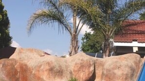 Una piscina cristalina con un tobogán azul y rocas grandes al fondo.