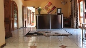 Un pasillo amplio con piso de baldosas, puertas de madera y una zona central con refrigerador y un florero.