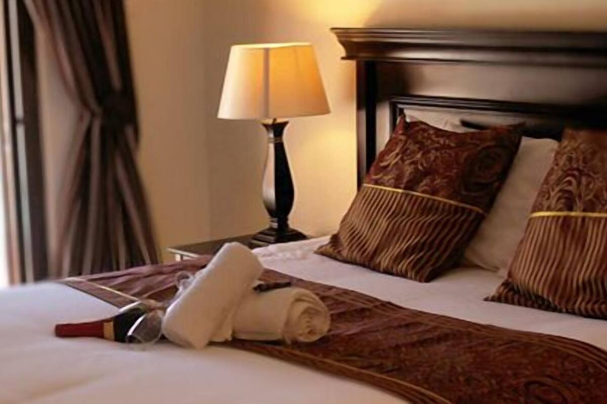 A hotel room with a neatly made bed, a bedside lamp, and a view of a swimming pool.