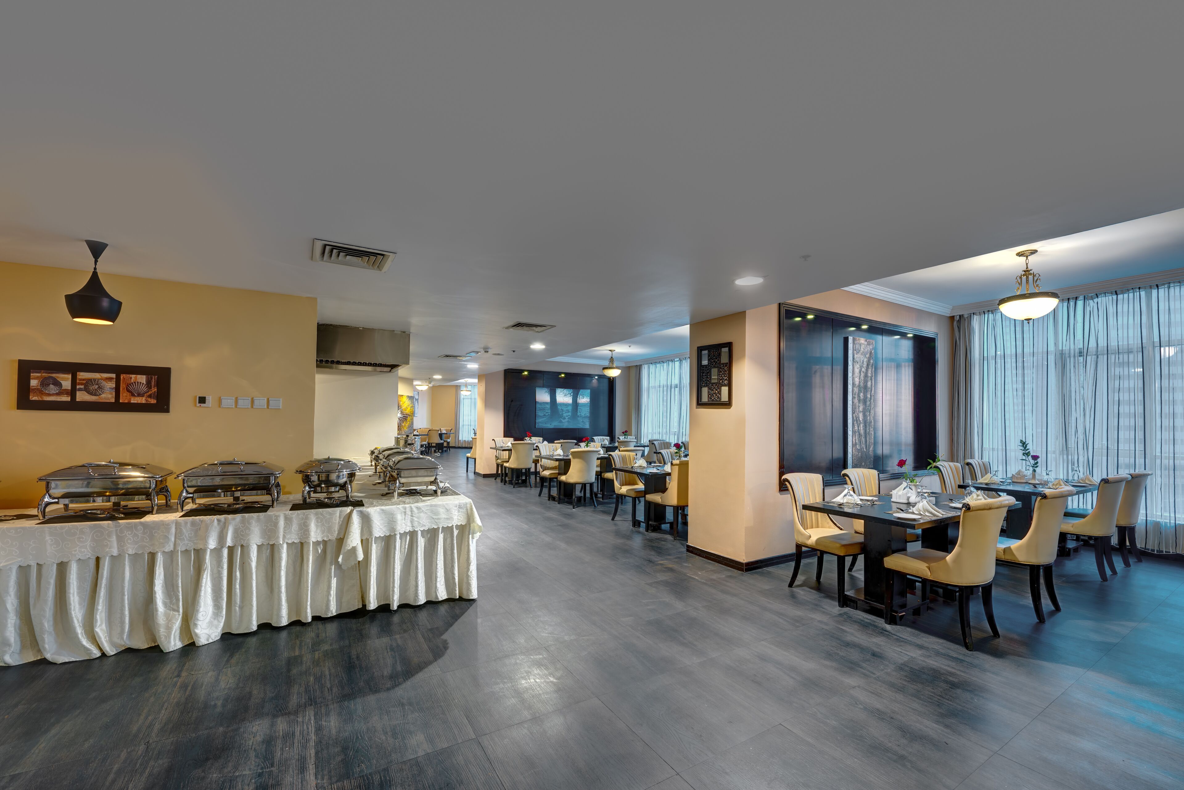 A spacious dining area with multiple tables and chairs, a buffet setup, and large windows providing natural light.