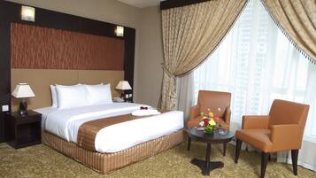 A hotel room with a large bed, two bedside tables with lamps, a small table with a vase of flowers, and a window with curtains.