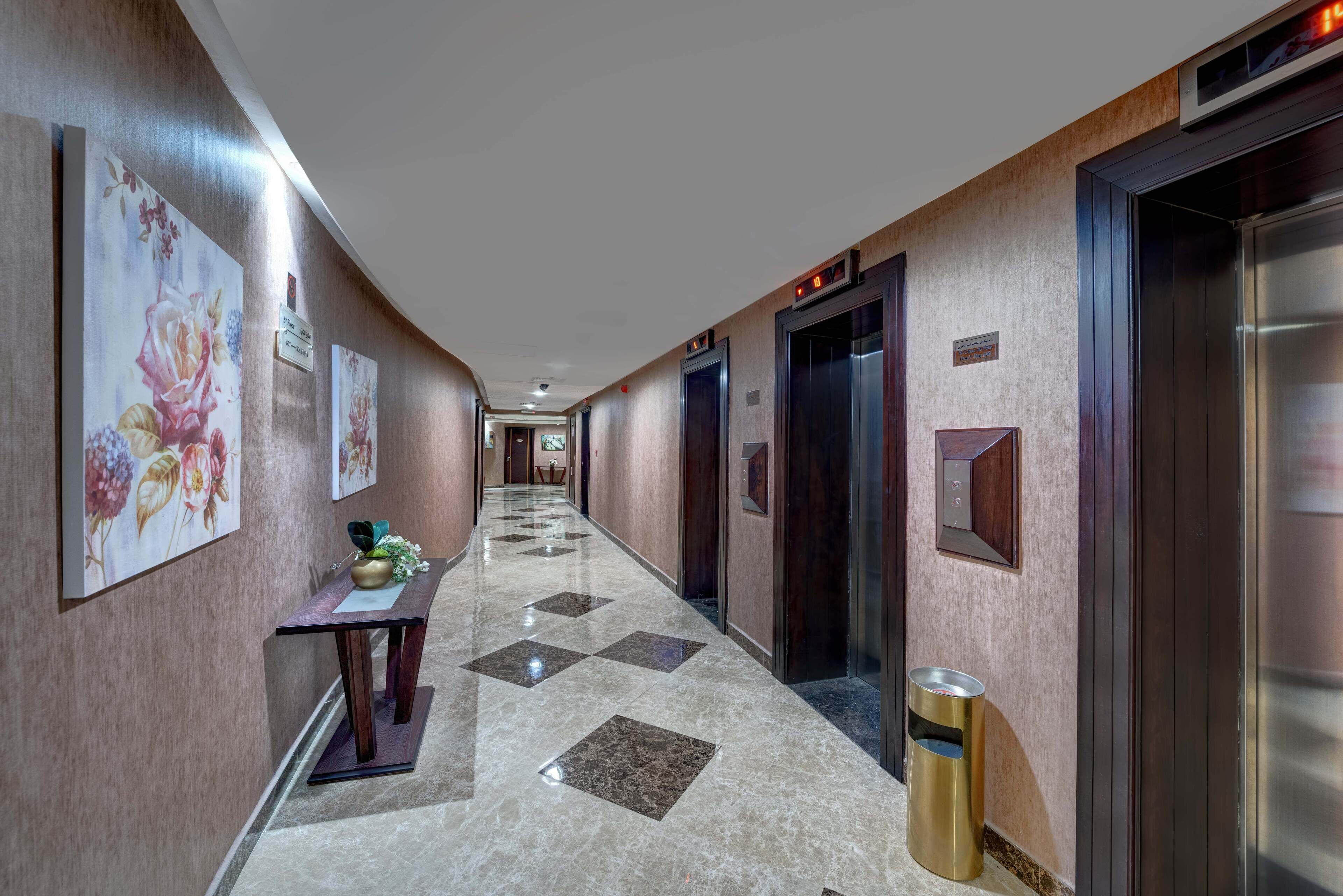A hotel hallway with a marble floor, floral wall art, a reception desk, and an elevator.