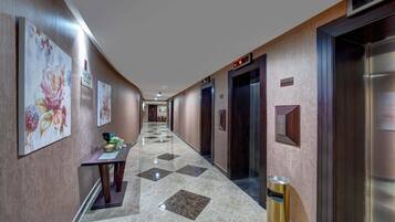A hotel hallway with a marble floor, floral wall art, a reception desk, and an elevator.