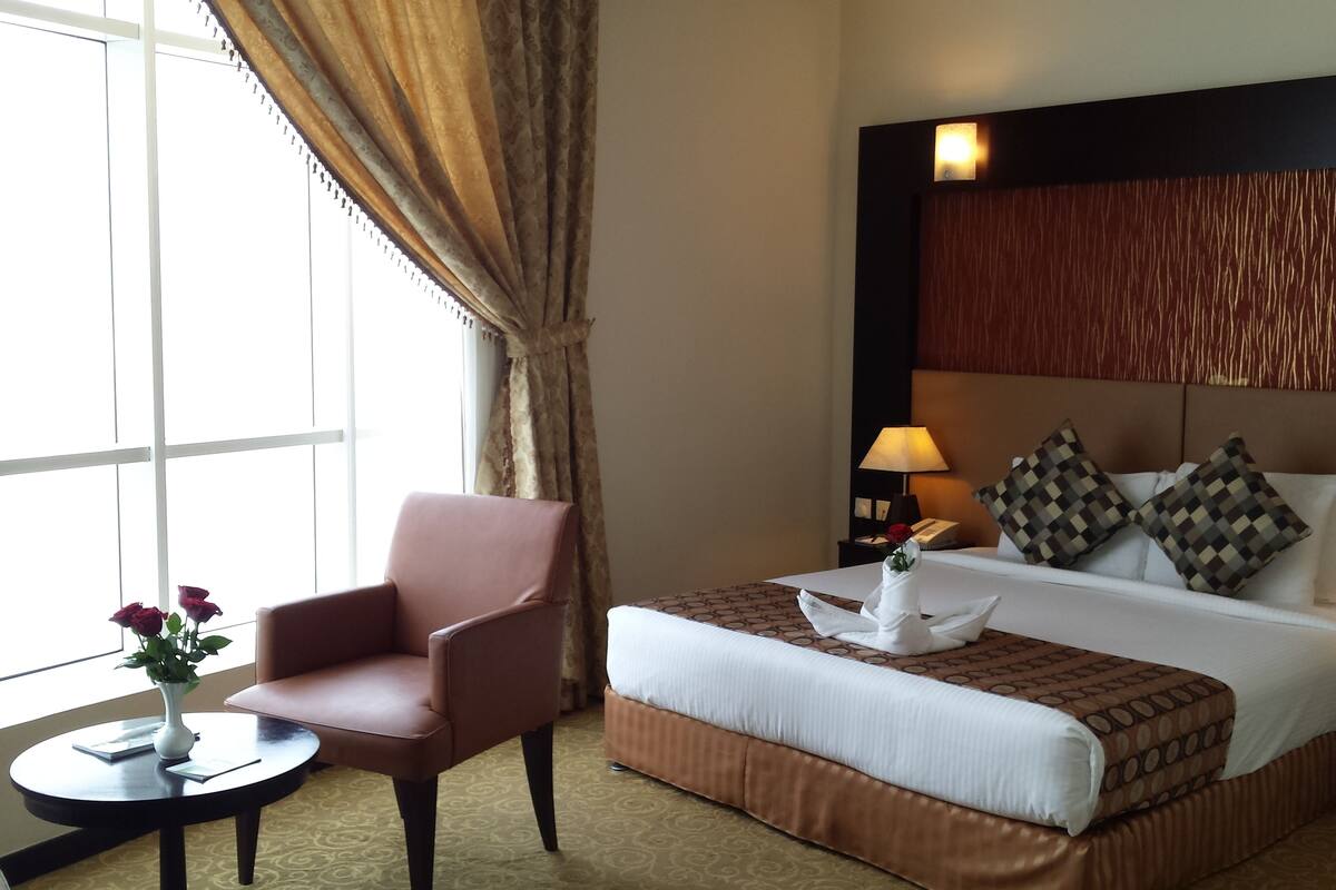 A hotel room with a large bed, a chair, a small table, and a vase with flowers.
