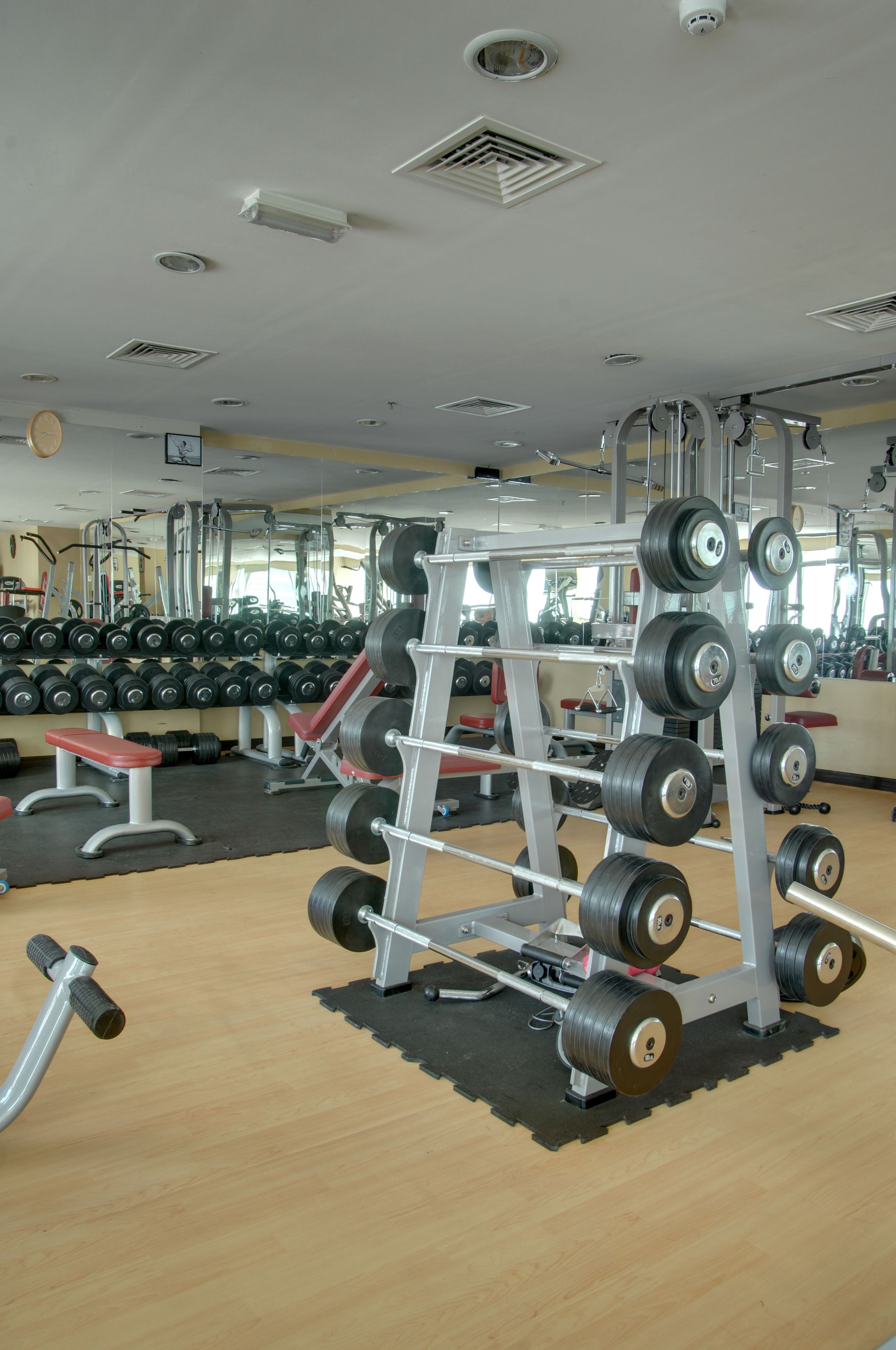 A gym with weightlifting equipment, mirrors, and a wooden floor.
