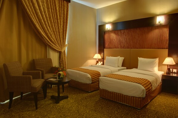 A hotel room with two beds, a sitting area with a chair and a small table, and a decorative vase with flowers.