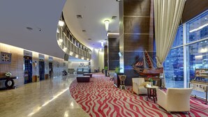 Eine geräumige Lobby mit einem rot-weißen Teppichmuster, modernen Möbeln und großen Fenstern mit Blick auf die Stadt.