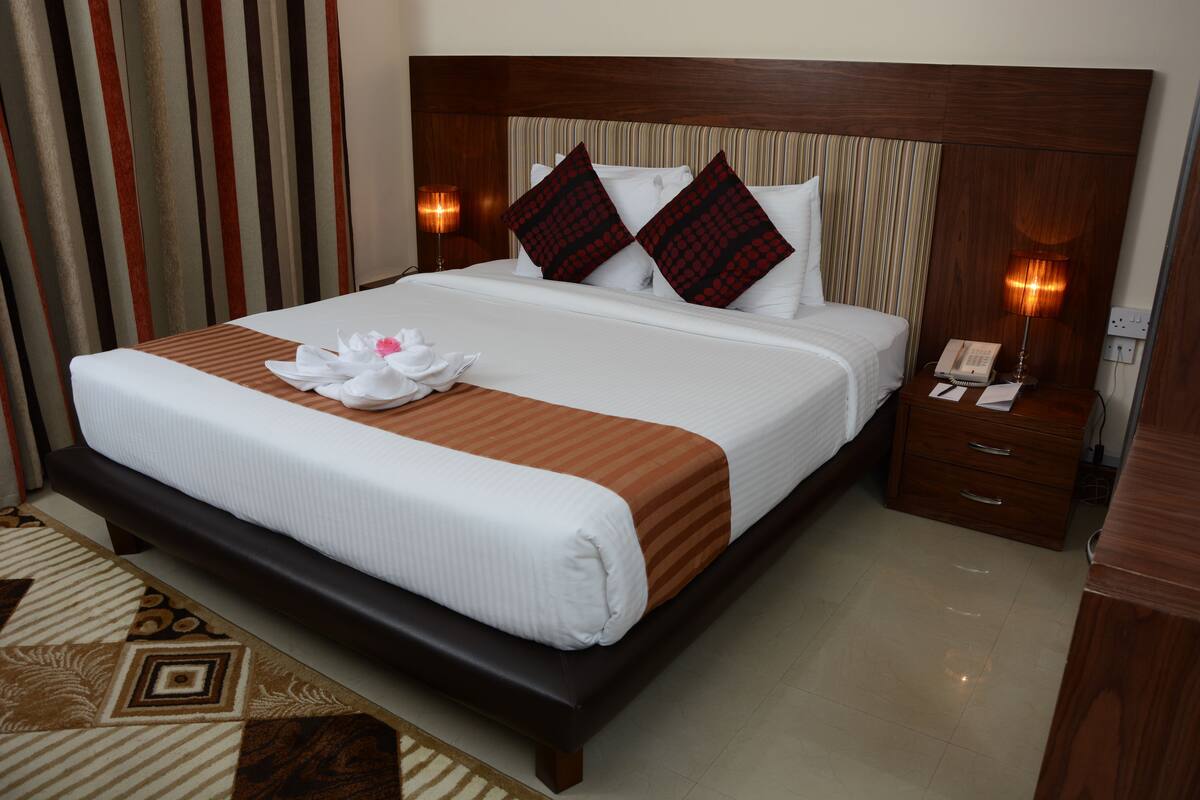A neatly made bed with a white and brown striped bedspread, two decorative pillows, a bedside table with a lamp, and a telephone.