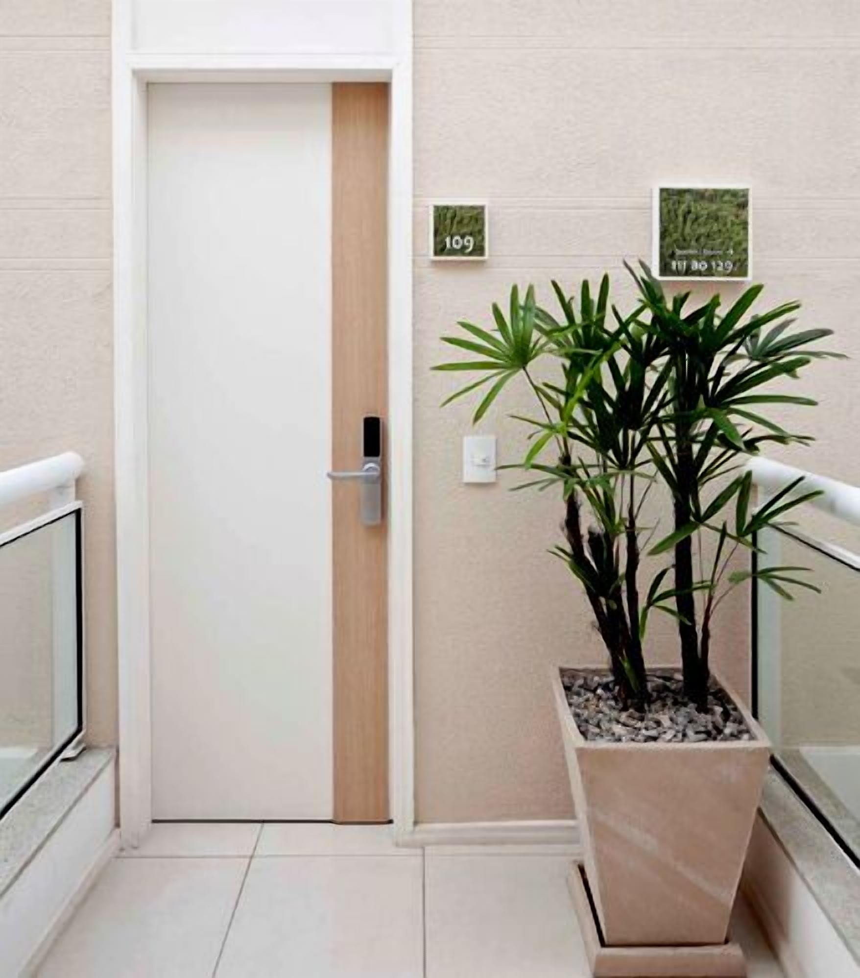 Un pasillo con una puerta cerrada, una planta en maceta y dos letreros en la pared.