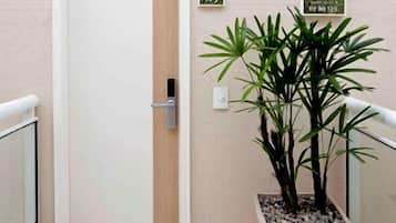 Un pasillo con una puerta cerrada, una planta en maceta y dos letreros en la pared.