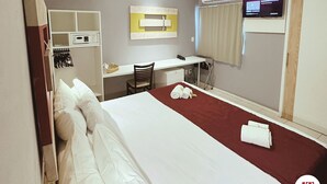 Une chambre d’hôtel équipée d’un lit, d’un bureau, d’une chaise, d’un climatiseur et d’un téléviseur.