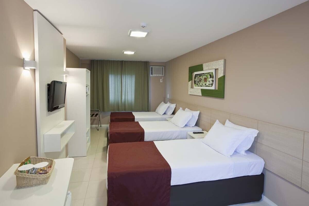 Habitación de hotel con dos camas, un televisor, una mesita con una cesta y un cuadro colgado en la pared.
