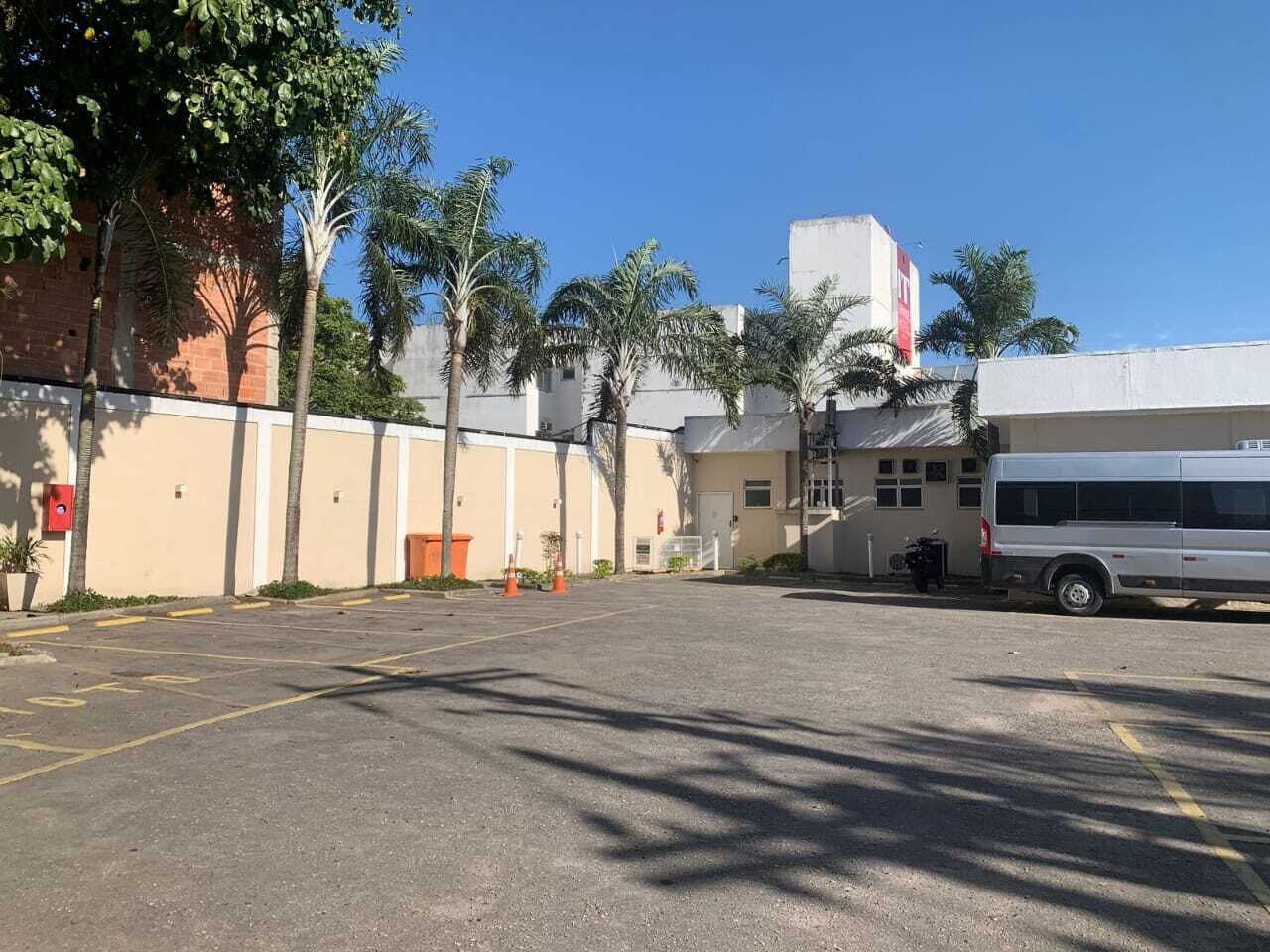 A parking lot with a white bus parked on the right, surrounded by palm trees and buildings.
