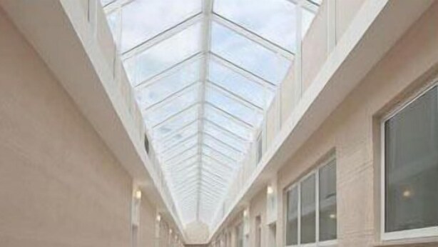 Un couloir doté d’un plafond haut et agrémenté d’une verrière aux motifs géométriques.