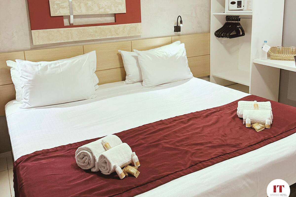 Una habitación de hotel con una cama, una manta roja, toallas enrolladas y artículos de aseo.