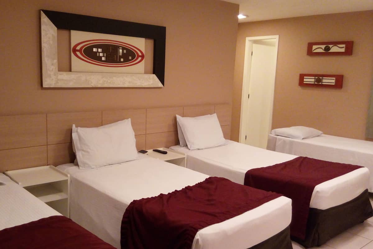 Una habitación de hotel con tres camas individuales, un cuadro en la pared y una puerta al fondo.