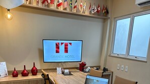 Une salle de conférence avec une longue table, des chaises, un ordinateur portable et un téléviseur affichant le logo du Grand Hôtel.