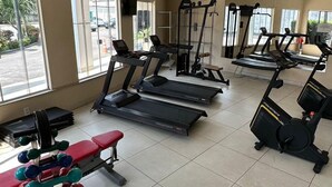 Une salle de sport équipée de tapis de course, de vélos elliptiques, d’un banc et d’un ensemble d’haltères.