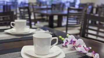 Un comedor con mesas y sillas, una taza blanca sobre un platillo, y una orquídea morada sobre la mesa.