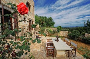 A stone building with a large red rose, outdoor seating, and a view of the landscape. - Strofilia Villas (Apokoronas)