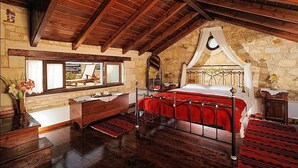 A bedroom with a wooden ceiling, stone walls, a four-poster bed, a wooden dresser, and a window with a view. - Strofilia Villas (Apokoronas)