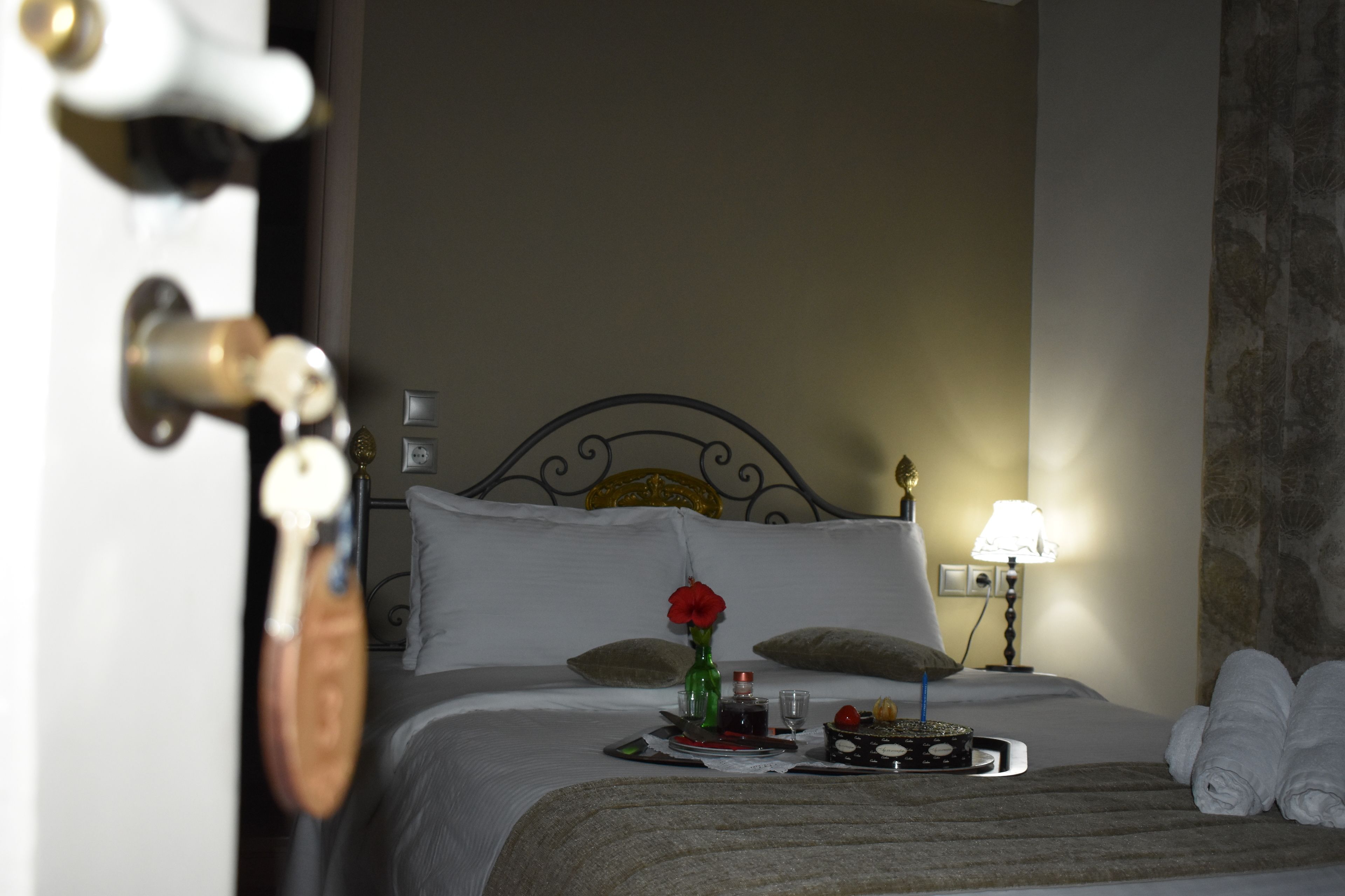 Une chambre d’hôtel avec un lit, des oreillers, une table de chevet avec une lampe, un vase avec une fleur et des serviettes sur le sol.