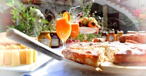 A table with a cheese platter, a pizza, and a fruit bowl with drinks.