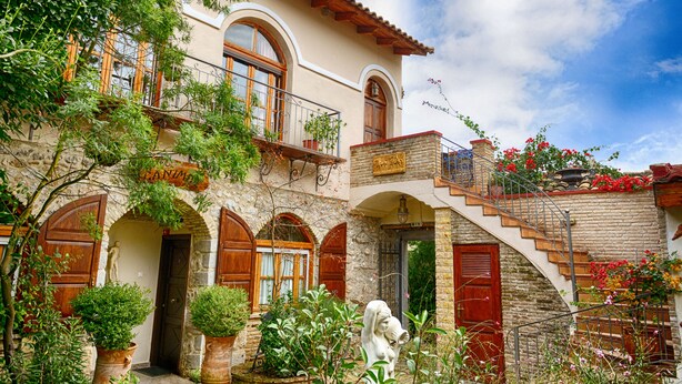 A traditional Mediterranean-style building with a stone facade, wooden shutters, and a balcony with potted plants. - Hotel Ganimede (Delphi)