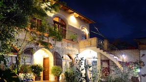 A well-lit, multi-story building with arched windows and balconies, surrounded by lush greenery. - Hotel Ganimede (Delphi)