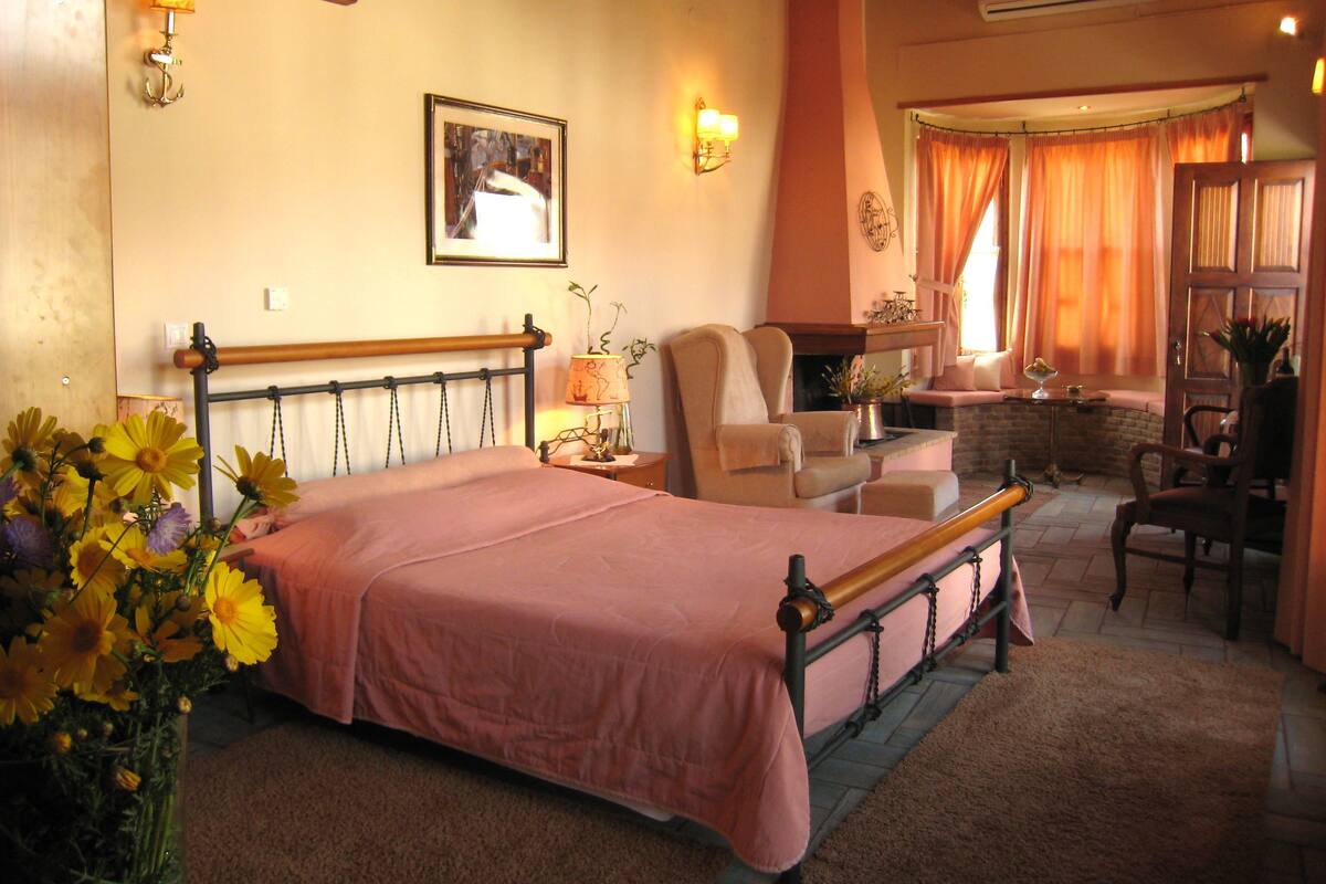 A bedroom with a bed, a chair, a table, and a window with curtains.