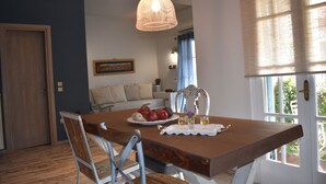 A dining area with a wooden table, chairs, and a hanging light fixture. A plate of fruit and a vase with flowers are on the table. - Hotel Ganimede (Delphi)