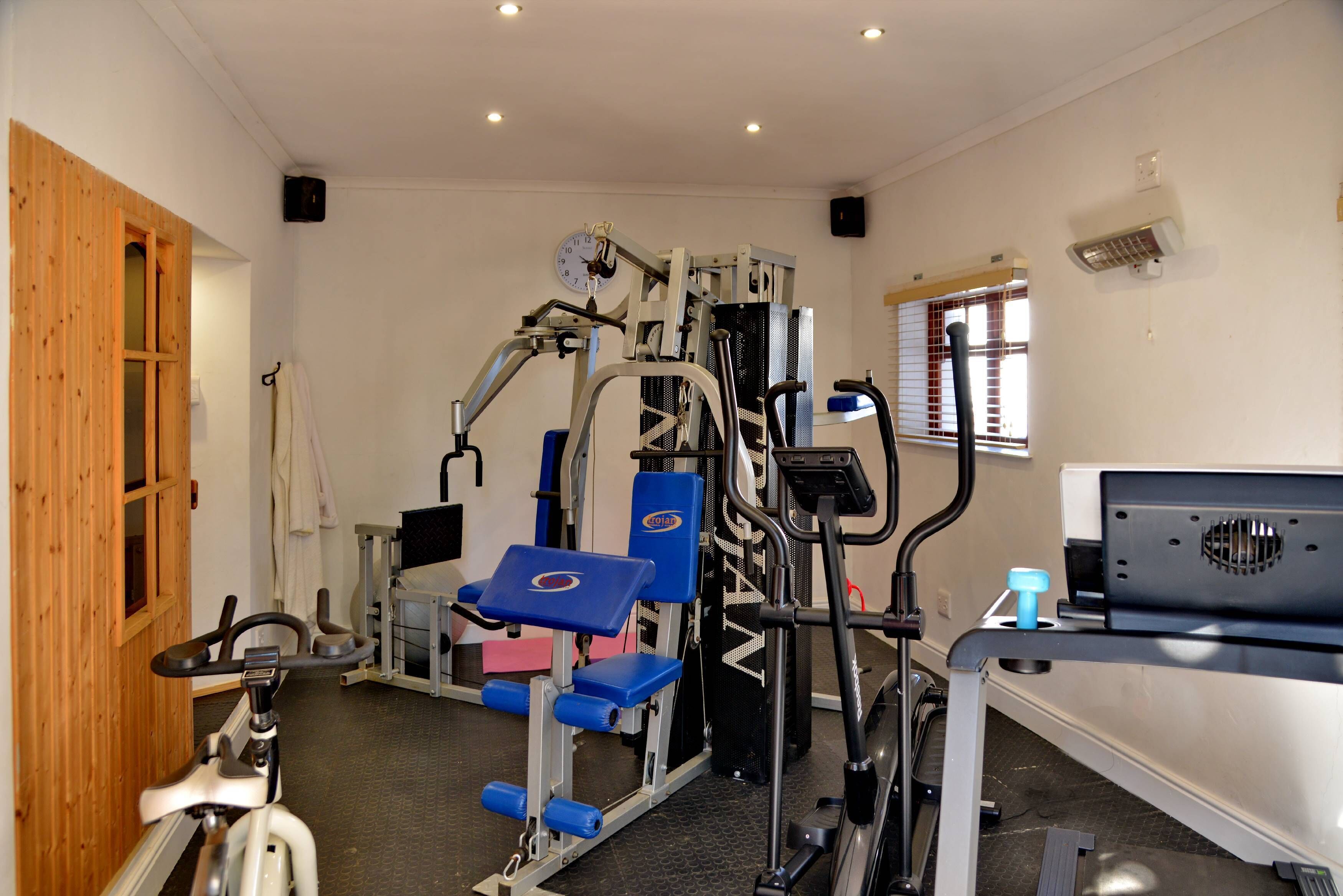 A gym with various exercise equipment, a wooden door, and a window with blinds.