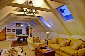 Une pièce mansardée avec une table de billard, des canapés jaunes, une table basse en bois et une grande fenêtre.