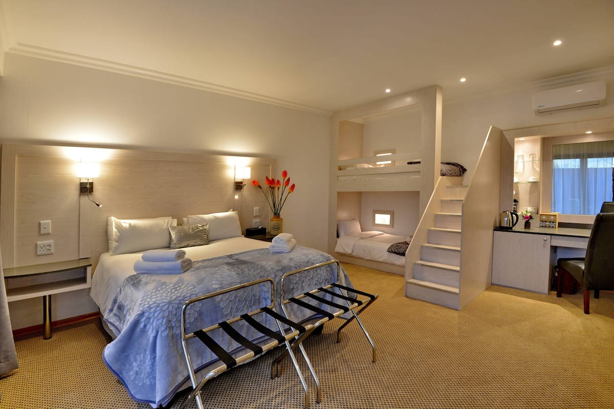 Een hotelkamer met een groot bed, een bureau, een stoel, een stapelbed en een trap.
