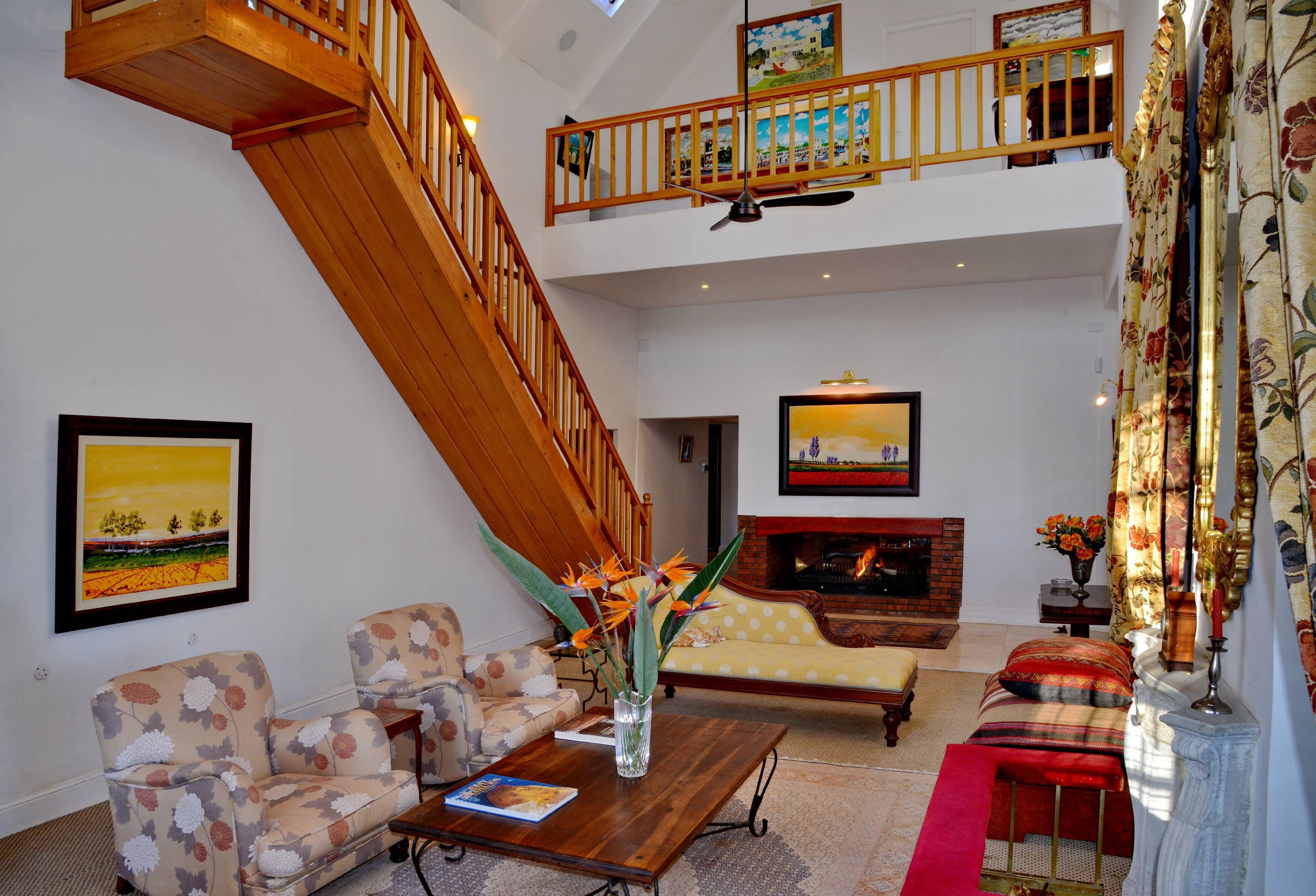 A spacious living room with a high wooden staircase, a fireplace, and a large painting on the wall.