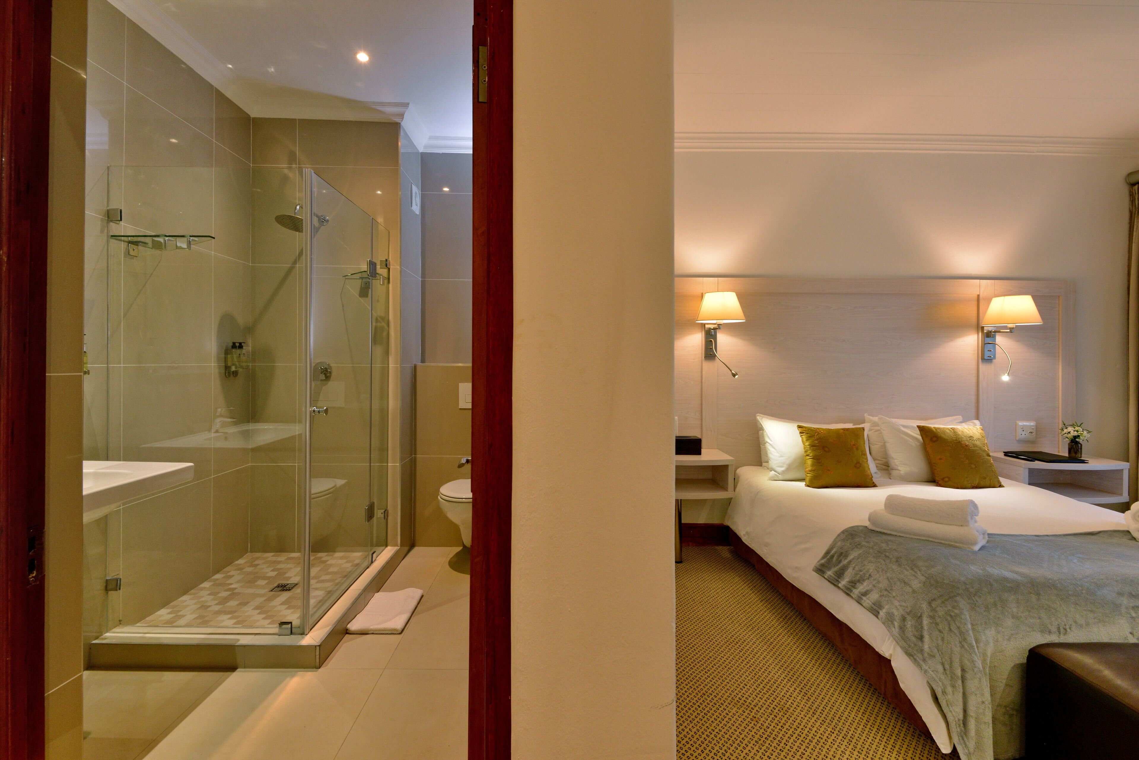 Une chambre d’hôtel avec une douche en verre, un lit avec une couette et des oreillers blancs, et des lampes de chevet.
