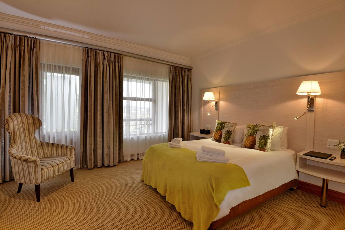 Een hotelkamer met een bed, een stoel, een nachtkastje en een lamp.