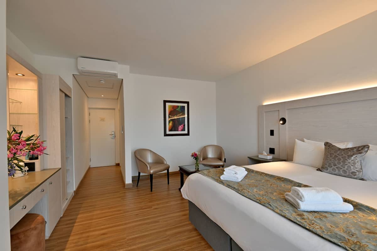Een hotelkamer met een bed, twee stoelen, een bureau en een kleine tafel met een bloevas.