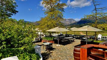 An outdoor patio with stone flooring, wooden tables and chairs, and umbrellas.
