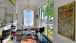 A modern interior with a chandelier, a dining area with white chairs, and a large window with a view of greenery. - Val Du Charron Wine & Leisure Estate (Wellington)